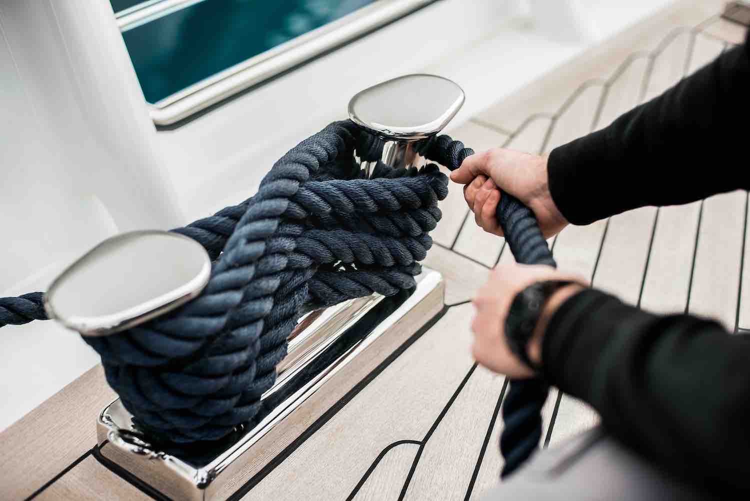 Detail of hands cleating off superyacht mooring lines on the foredeck with teak deck and stainless steel fittings